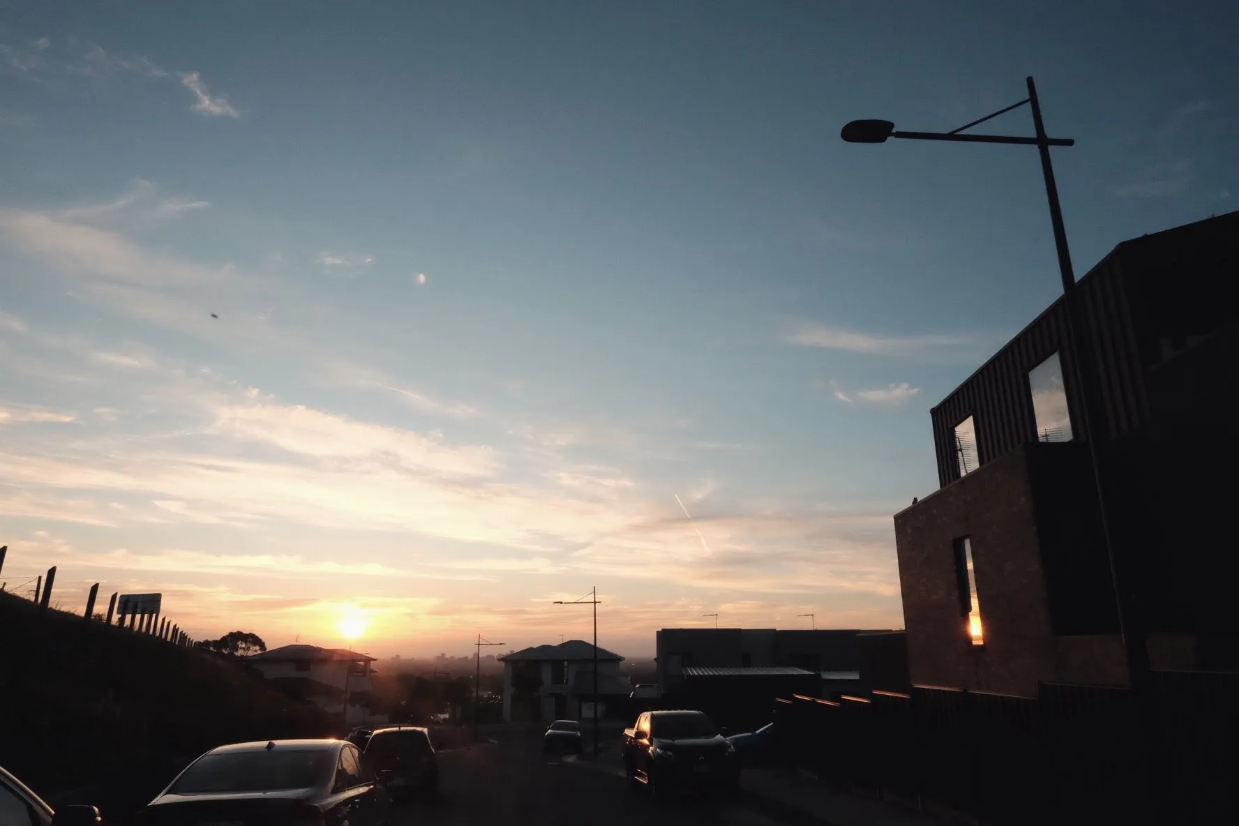 Sunset over suburban rooftops with a streetlight silhouette